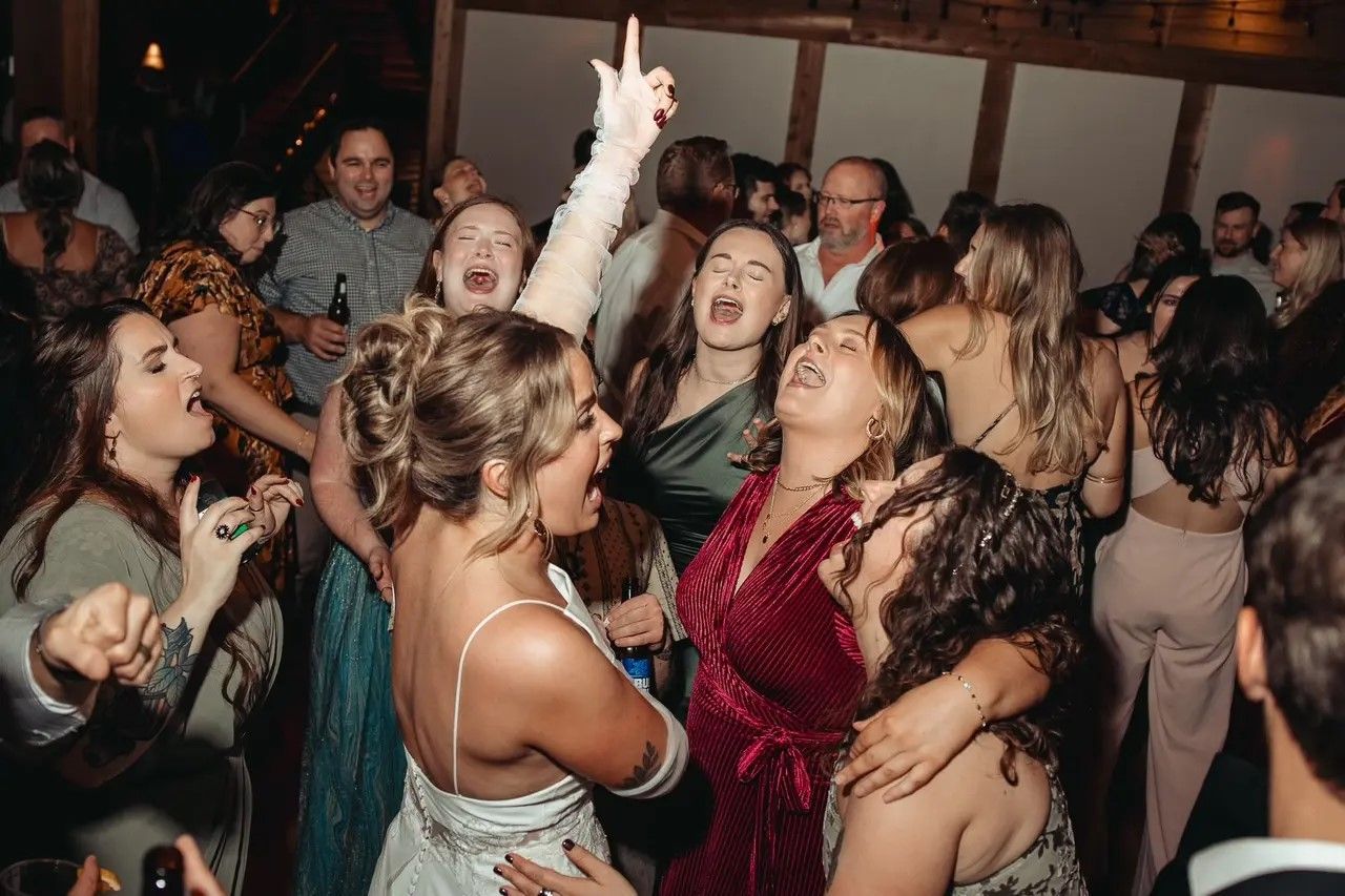 People dancing and celebrating at a wedding reception; indoor setting with dim lighting.