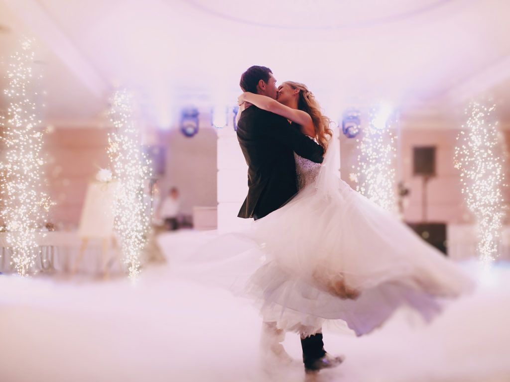 Couple dancing, embracing, celebrating wedding. Sparklers, ballroom setting, bright, romantic.