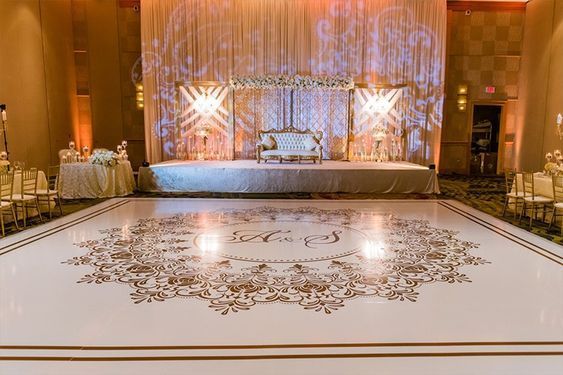 Formal event setup, featuring a white stage, golden decorations, and a dance floor with a custom monogram.