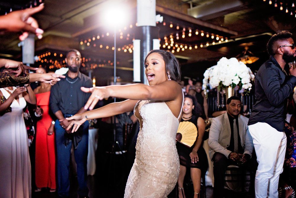 Woman dancing in a gold dress at a party, arms outstretched. People surround her.