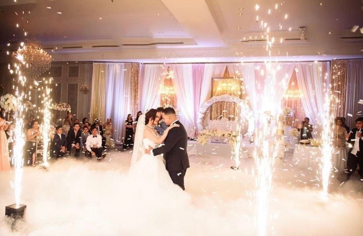Couple dancing at wedding with sparklers and fog. Guests watch in background.