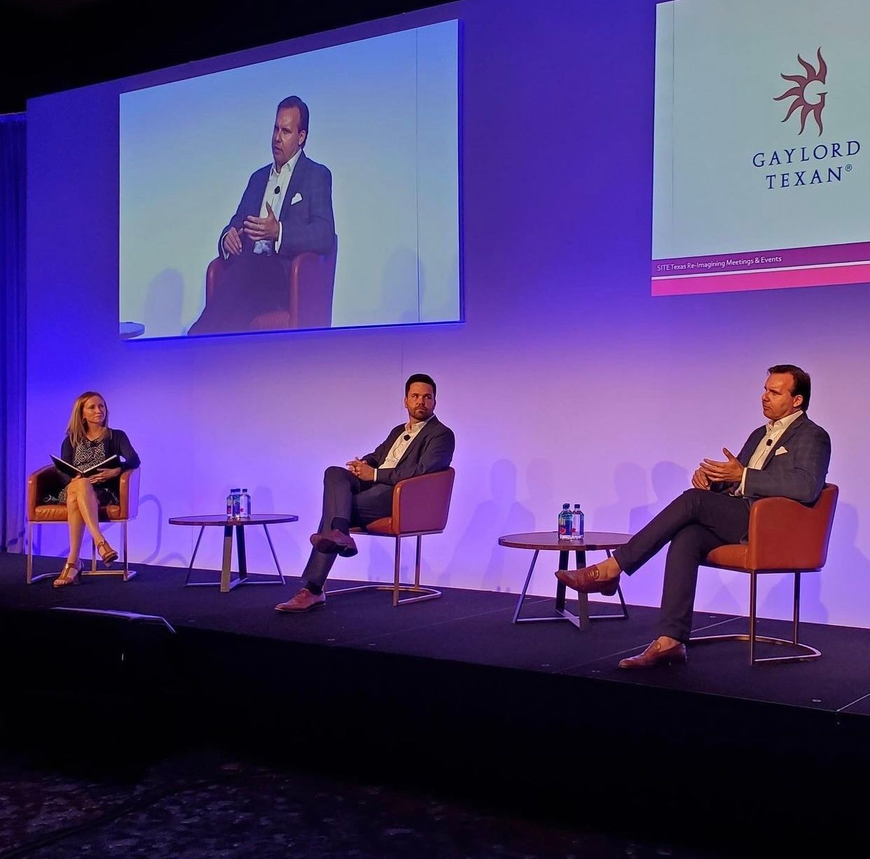 A group of people are sitting on a stage in front of a screen.