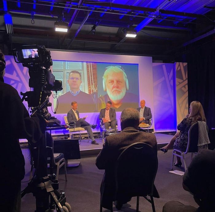A panel discussion takes place on a stage with a large screen displaying 