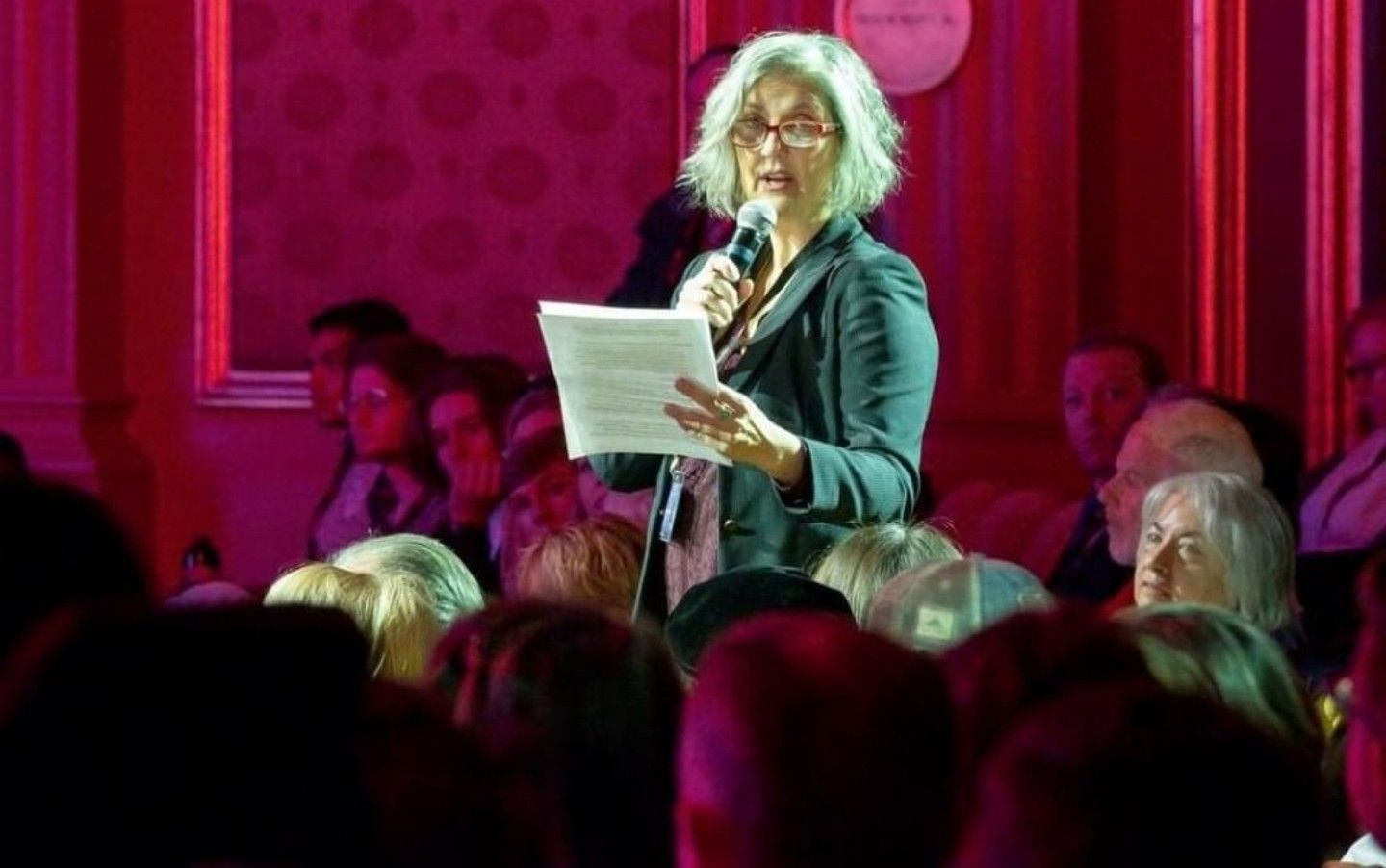 A woman is speaking into a microphone in front of a crowd.