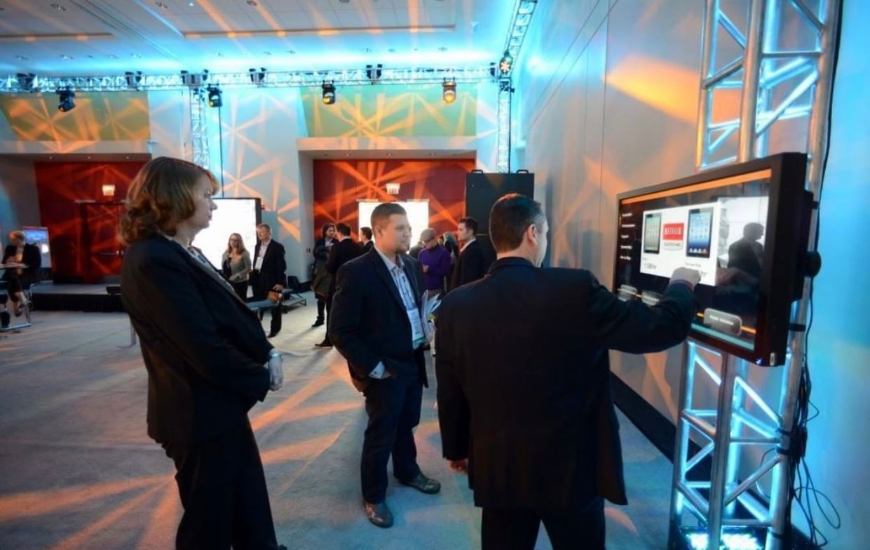 A group of people are standing around a large screen in a room.