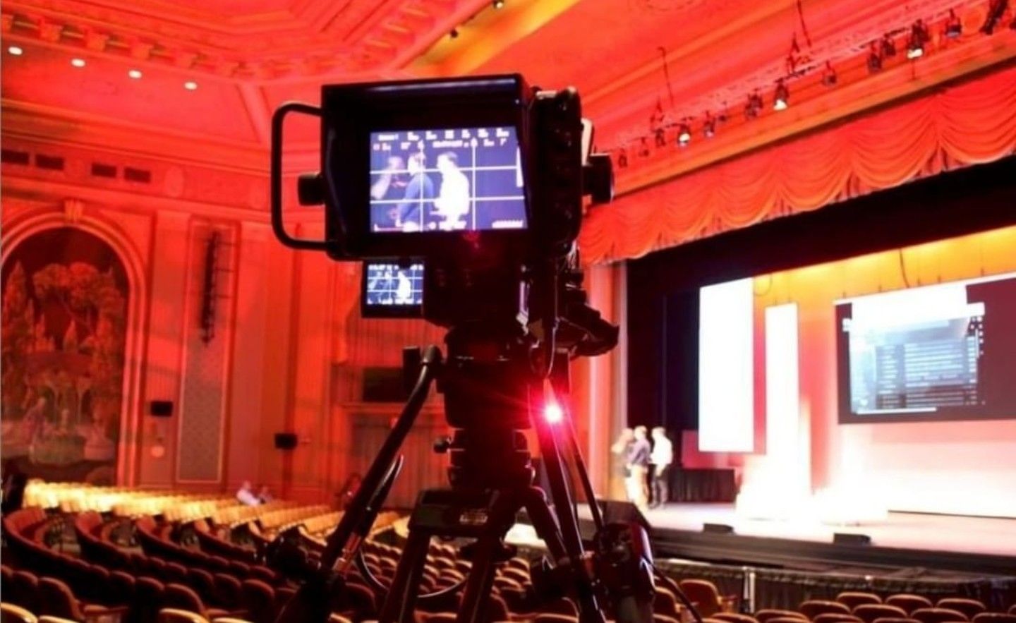 A camera is sitting on a tripod in an auditorium.