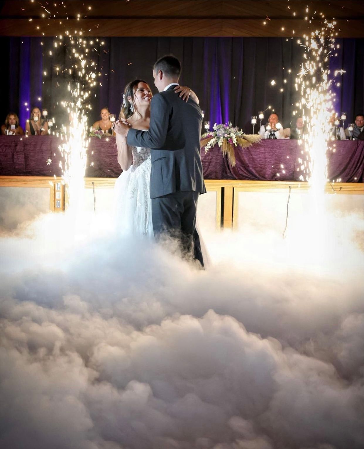 A bride and groom are dancing in the fog at their wedding reception.