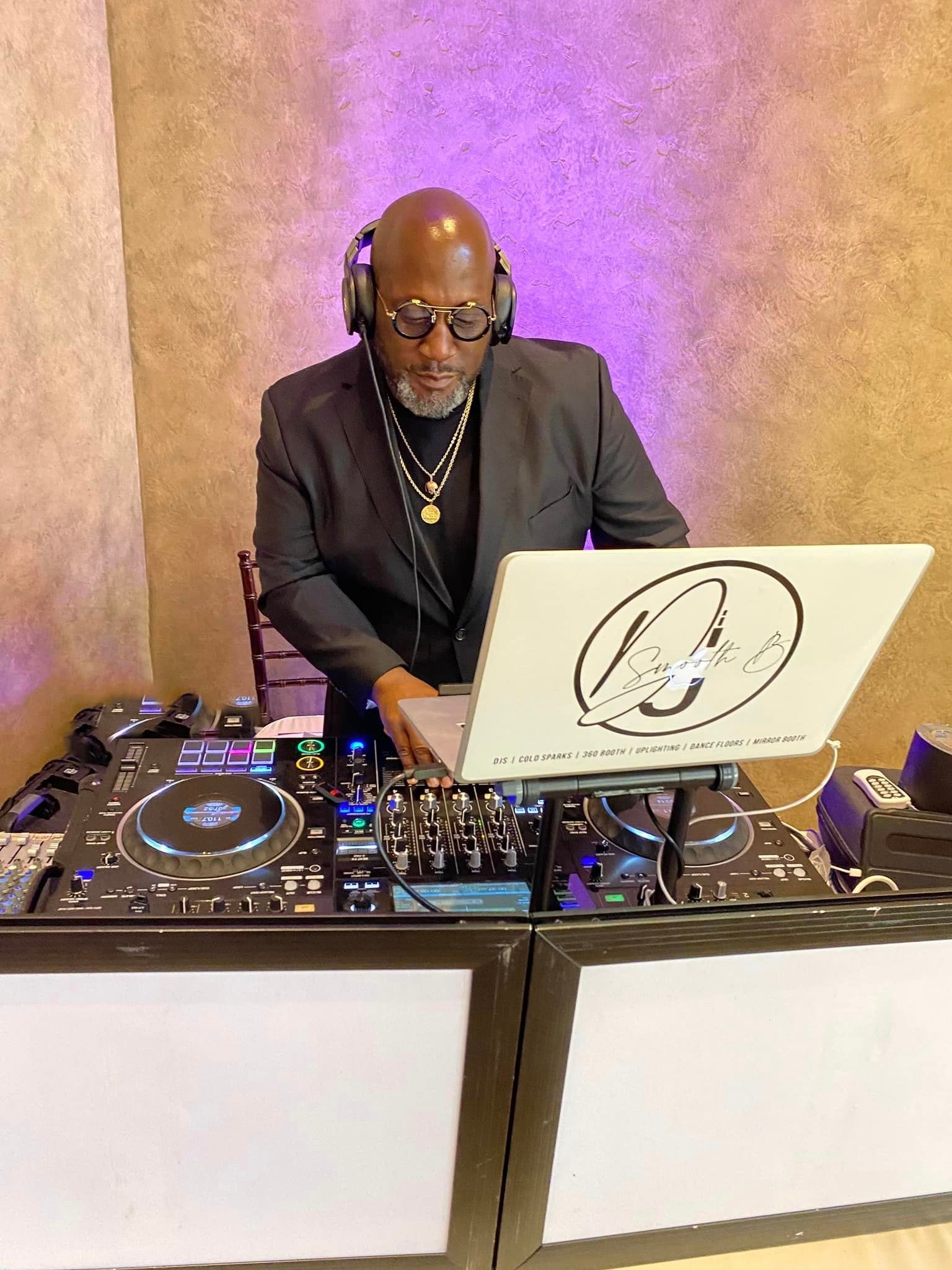 A man in a suit and headphones is playing music on a laptop.
