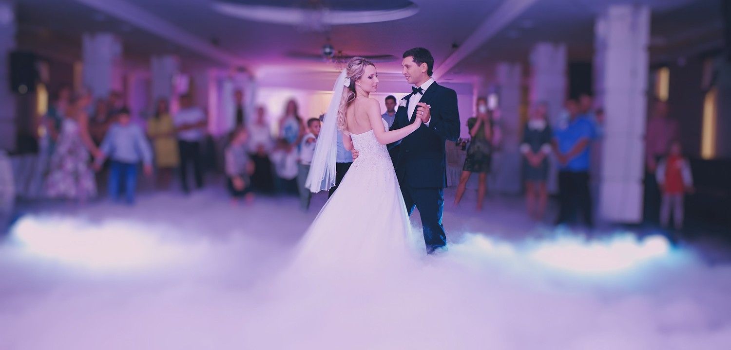 A bride and groom are dancing in the fog at their wedding reception.