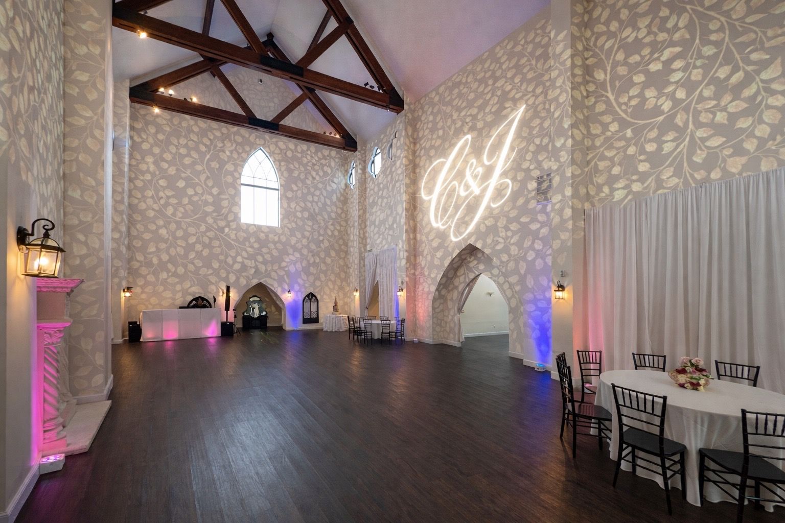 Elegant empty event hall with dark wood floors, white patterned walls, and purple accent lighting