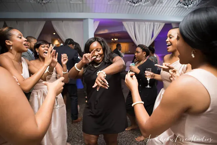 People dancing joyfully at a party, inside a venue with white curtains and ambient lighting.