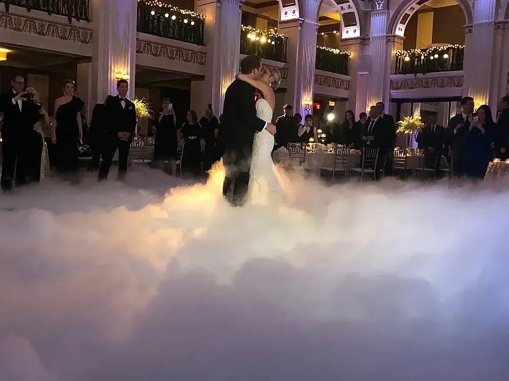 Bride and groom dance on a cloud of fog at a wedding reception. Elegant ballroom with guests watching.