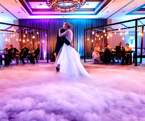 Bride and groom dance on a cloud of fog at their wedding reception, purple lighting.