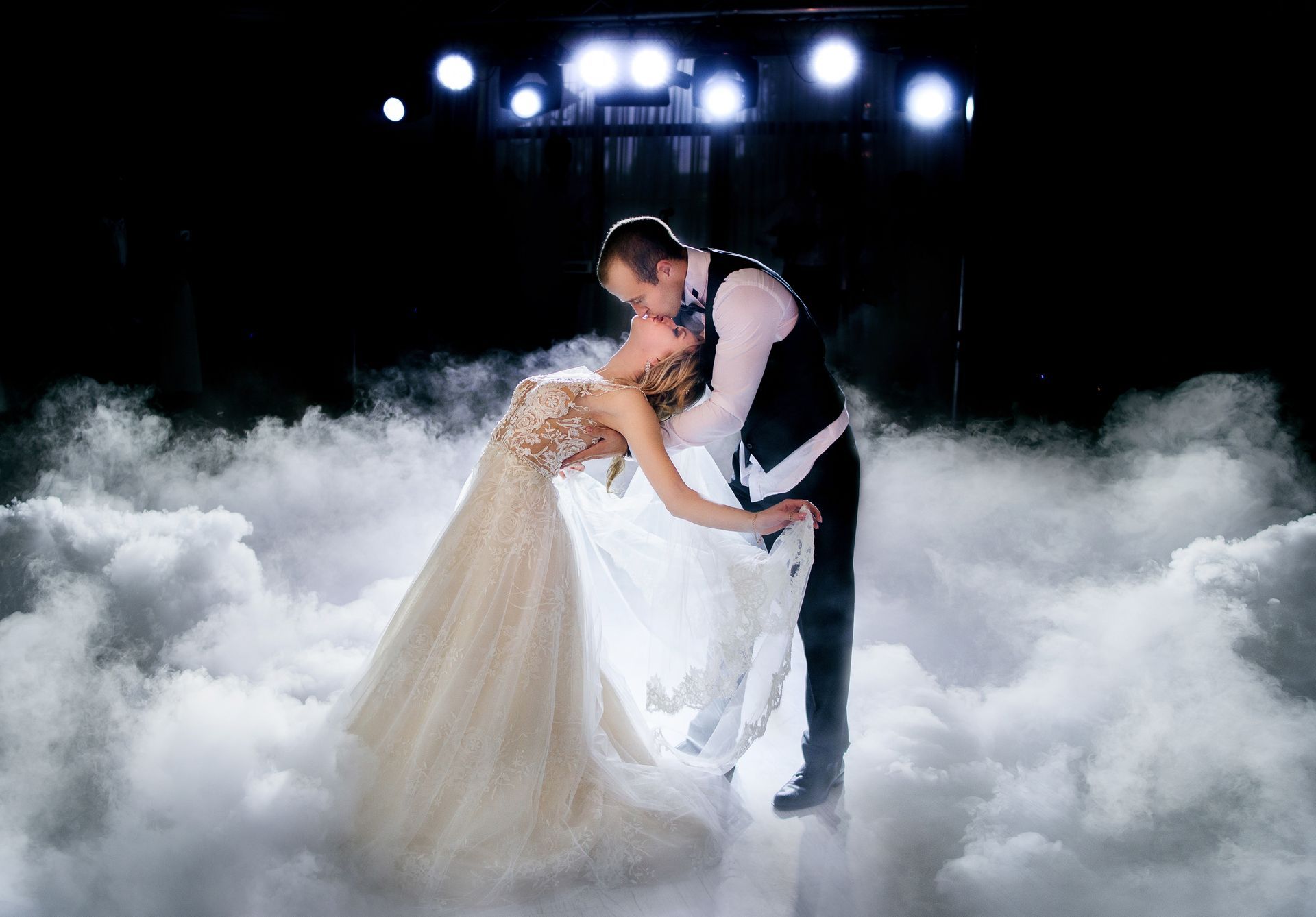 Couple kissing on a cloud of smoke, lit by overhead lights, formal attire.