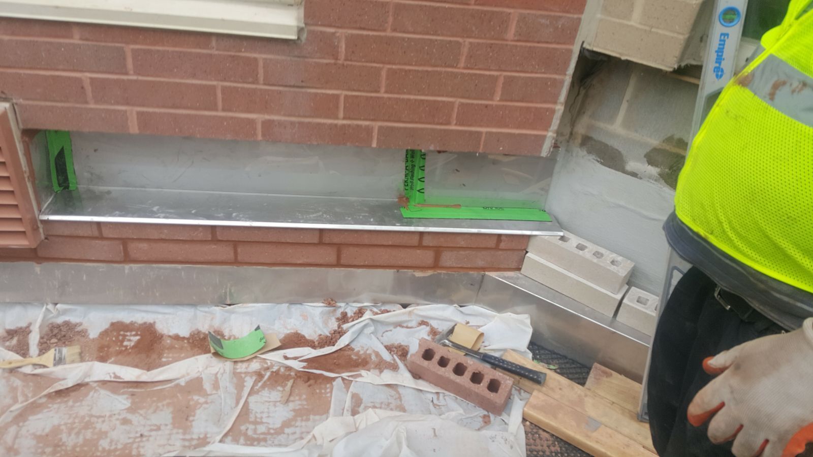 A man in a yellow vest is working on a brick wall.