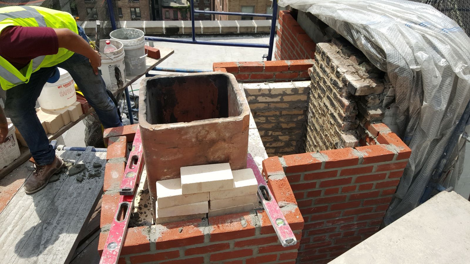 A construction worker is working on a brick chimney.