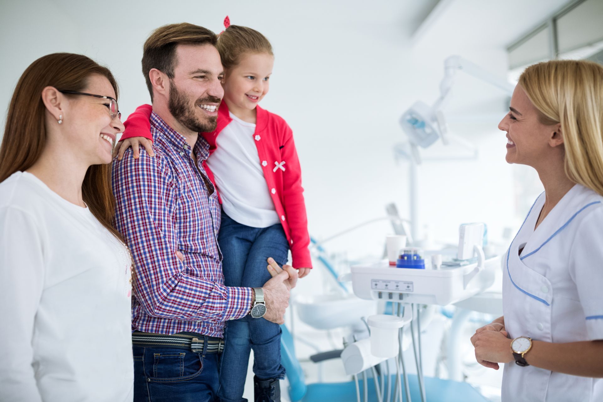 Adult holding child speaking with dental professional in clinic exam room. Adult holding child speaking with dental professional in clinic exam room.