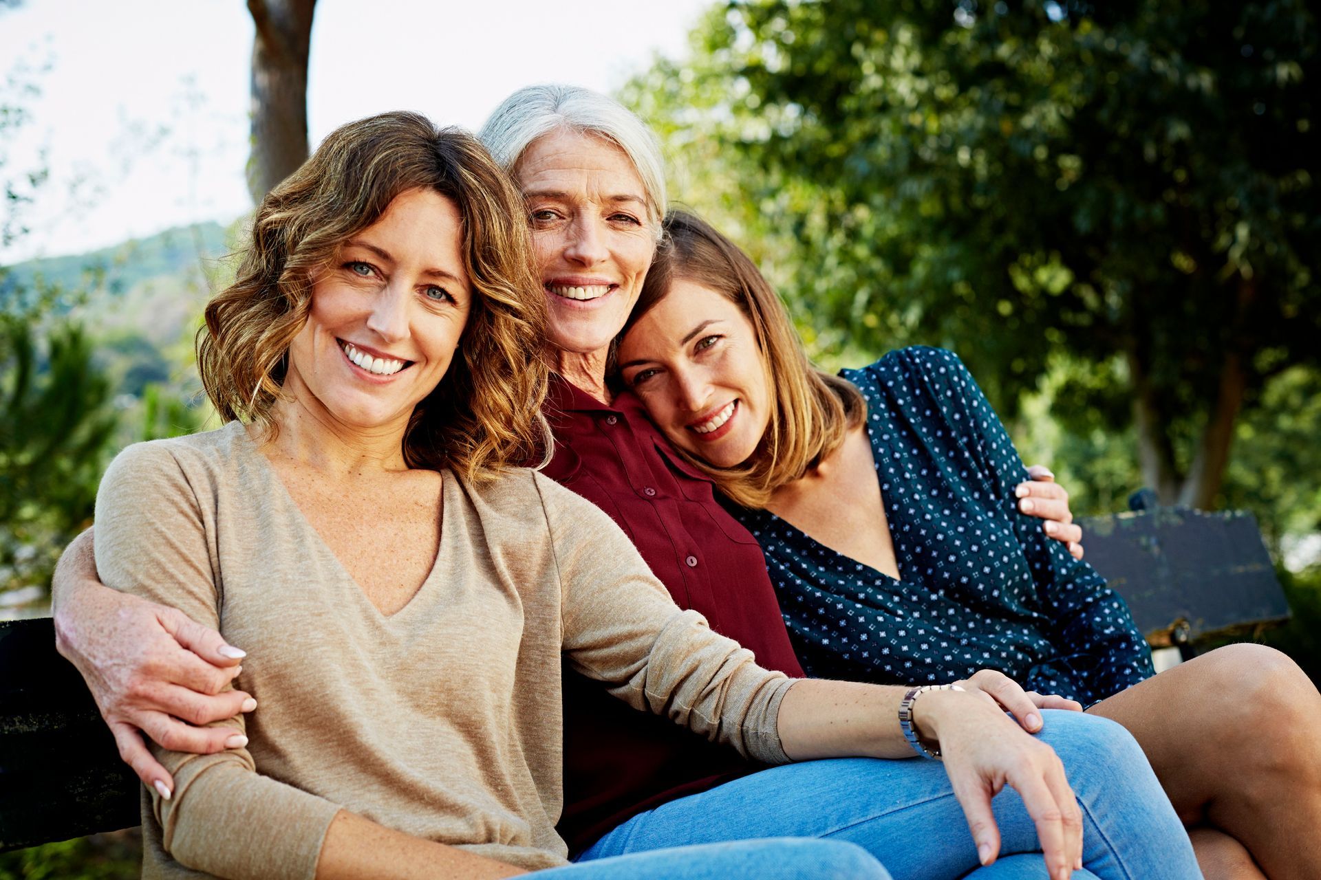 A woman is sitting on a couch with two little girls hugging her.