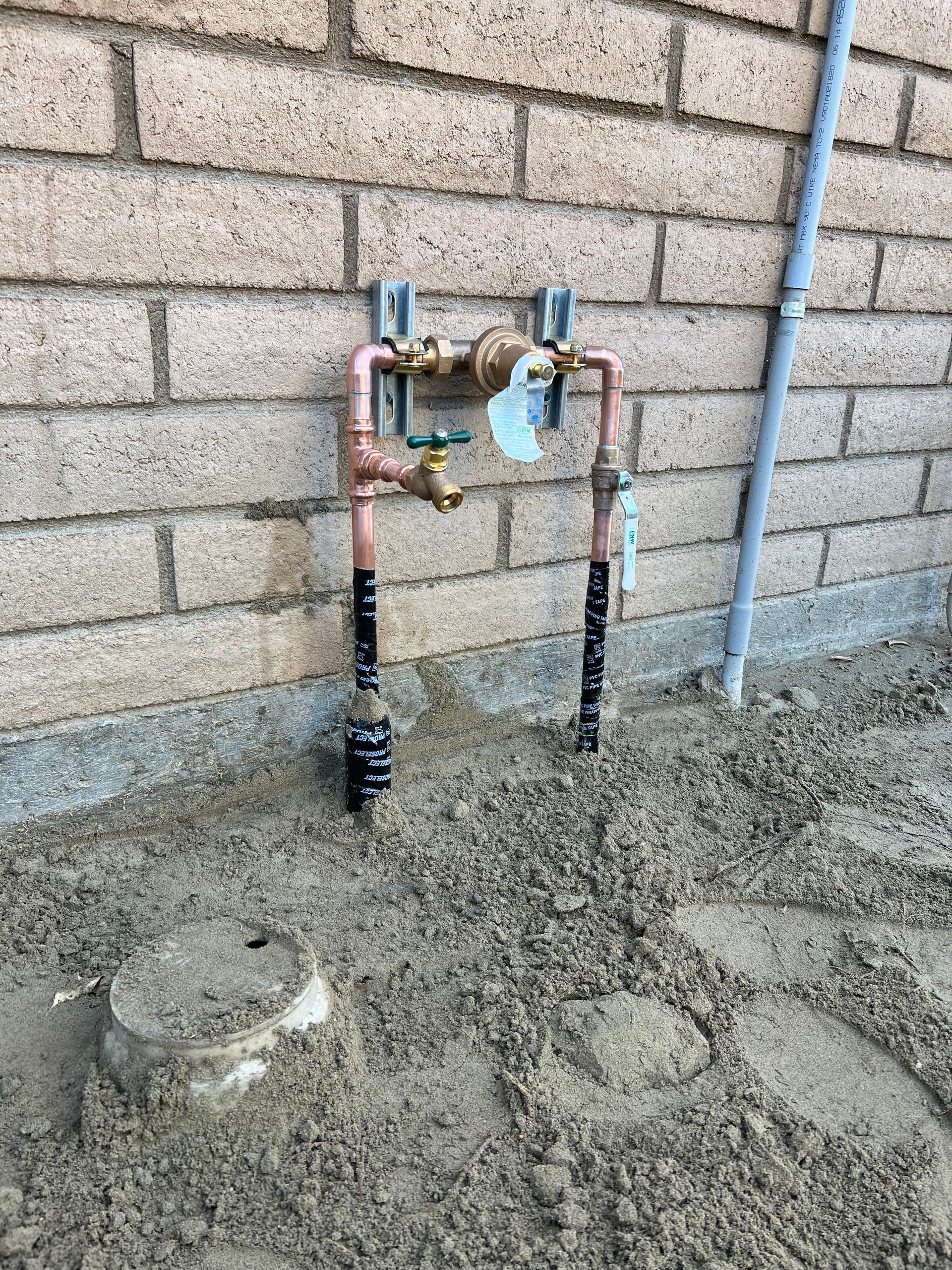 A water faucet is sitting on the ground next to a brick wall.