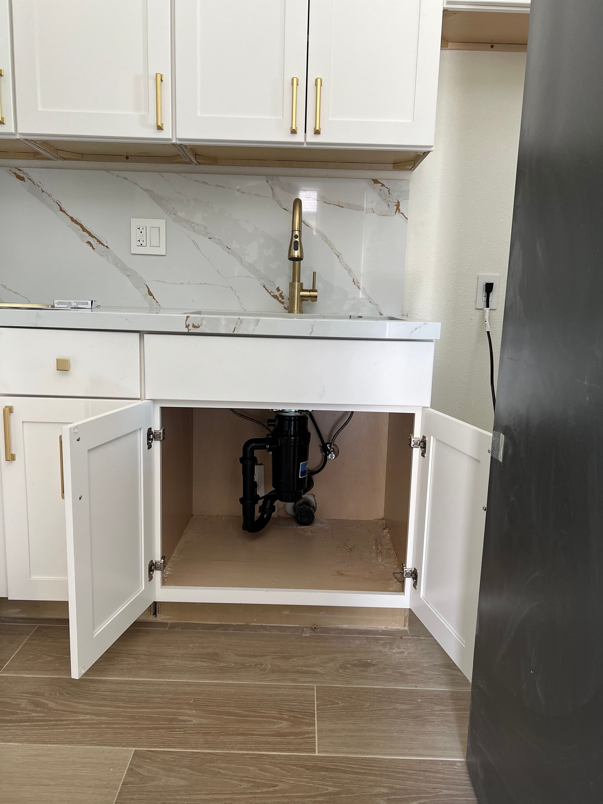 A kitchen sink with a faucet and cabinets open.