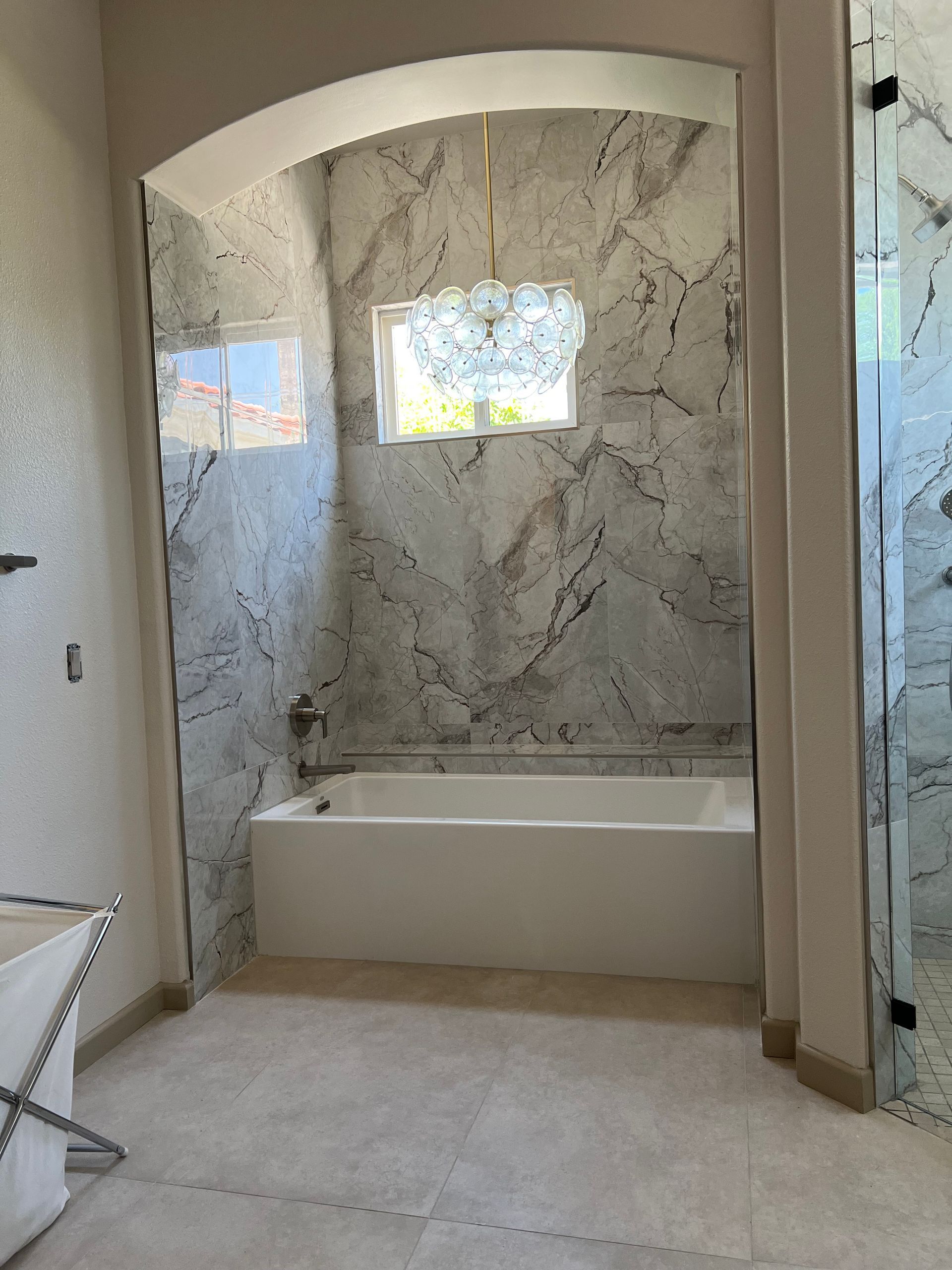 A bathroom with a tub and a shower with marble walls.