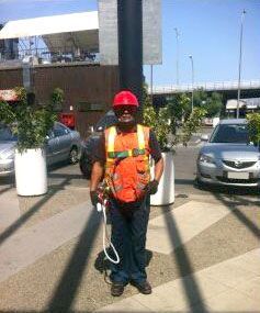 Un hombre que lleva casco y chaleco de seguridad está parado frente a un poste.