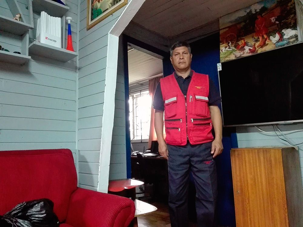 Un hombre con un chaleco rojo está de pie en una sala de estar al lado de una silla roja.