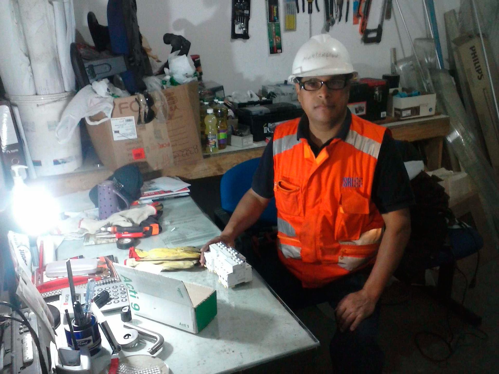 Un hombre que lleva un chaleco naranja y un casco está sentado en un escritorio.