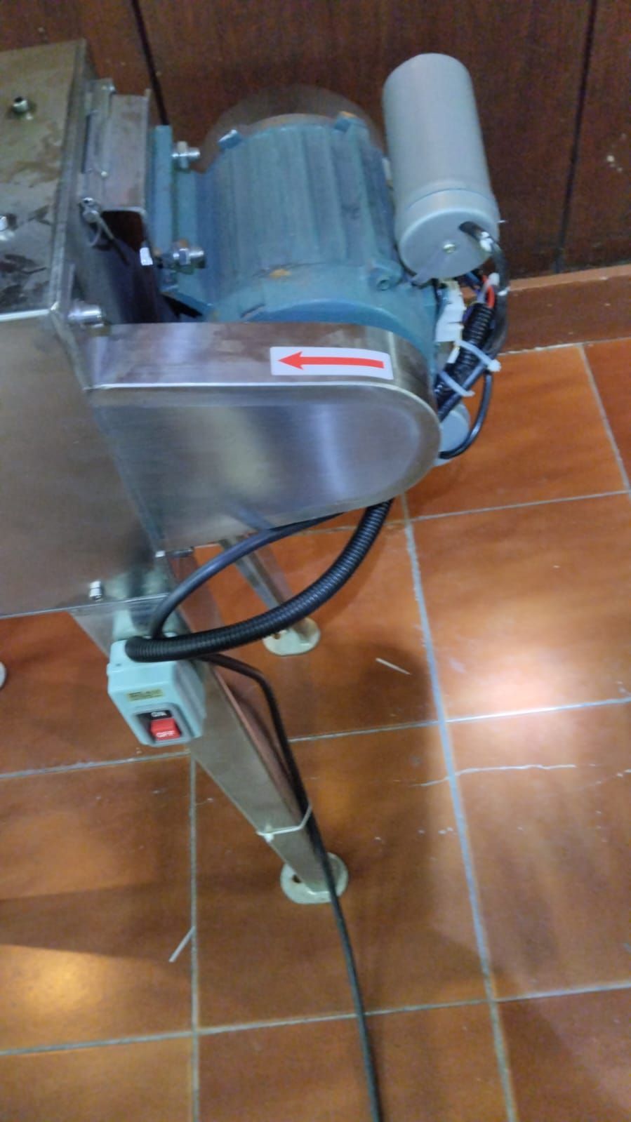 Una máquina de acero inoxidable con un motor acoplado se encuentra sobre un suelo de baldosas.