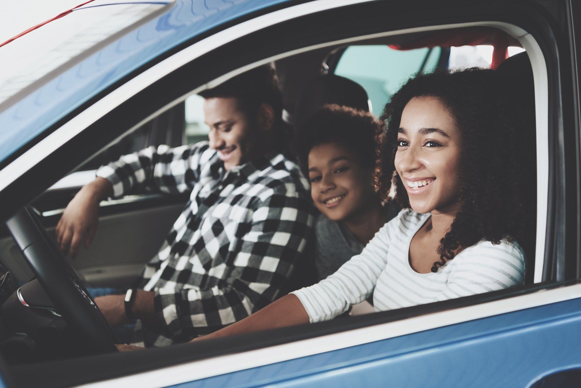 A family is sitting in a car and smiling.