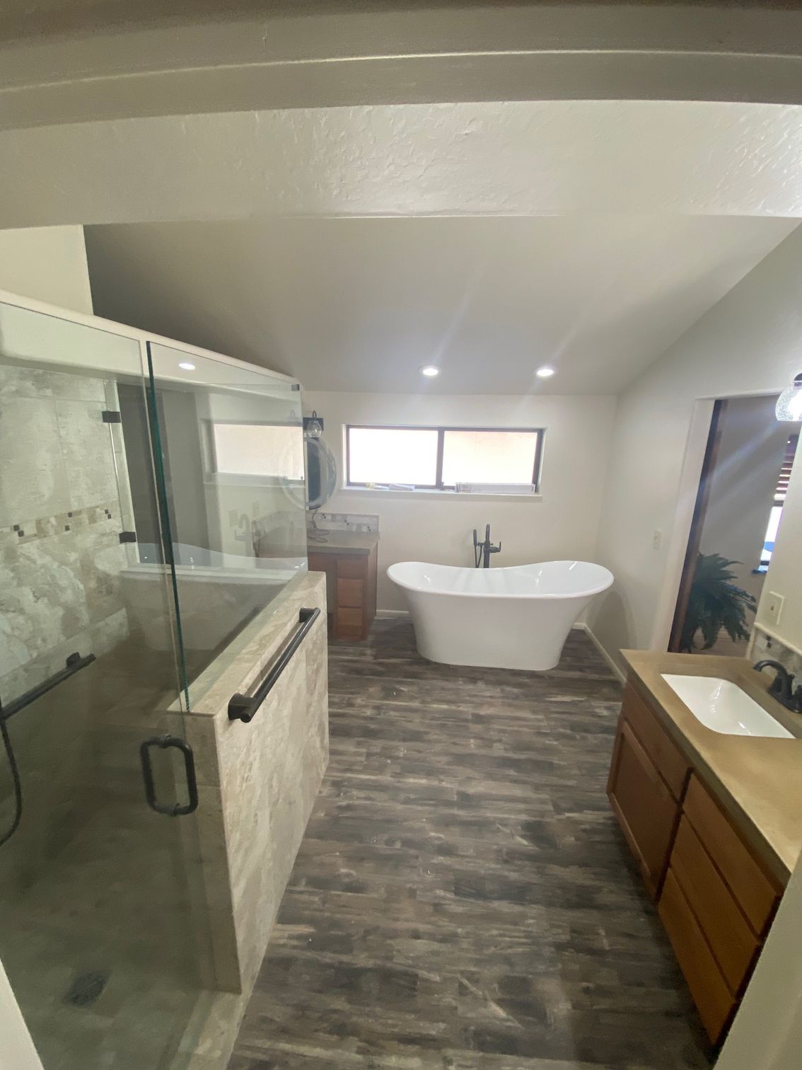 Modern bathroom with a glass shower, soaking tub, wood vanity, and a window.