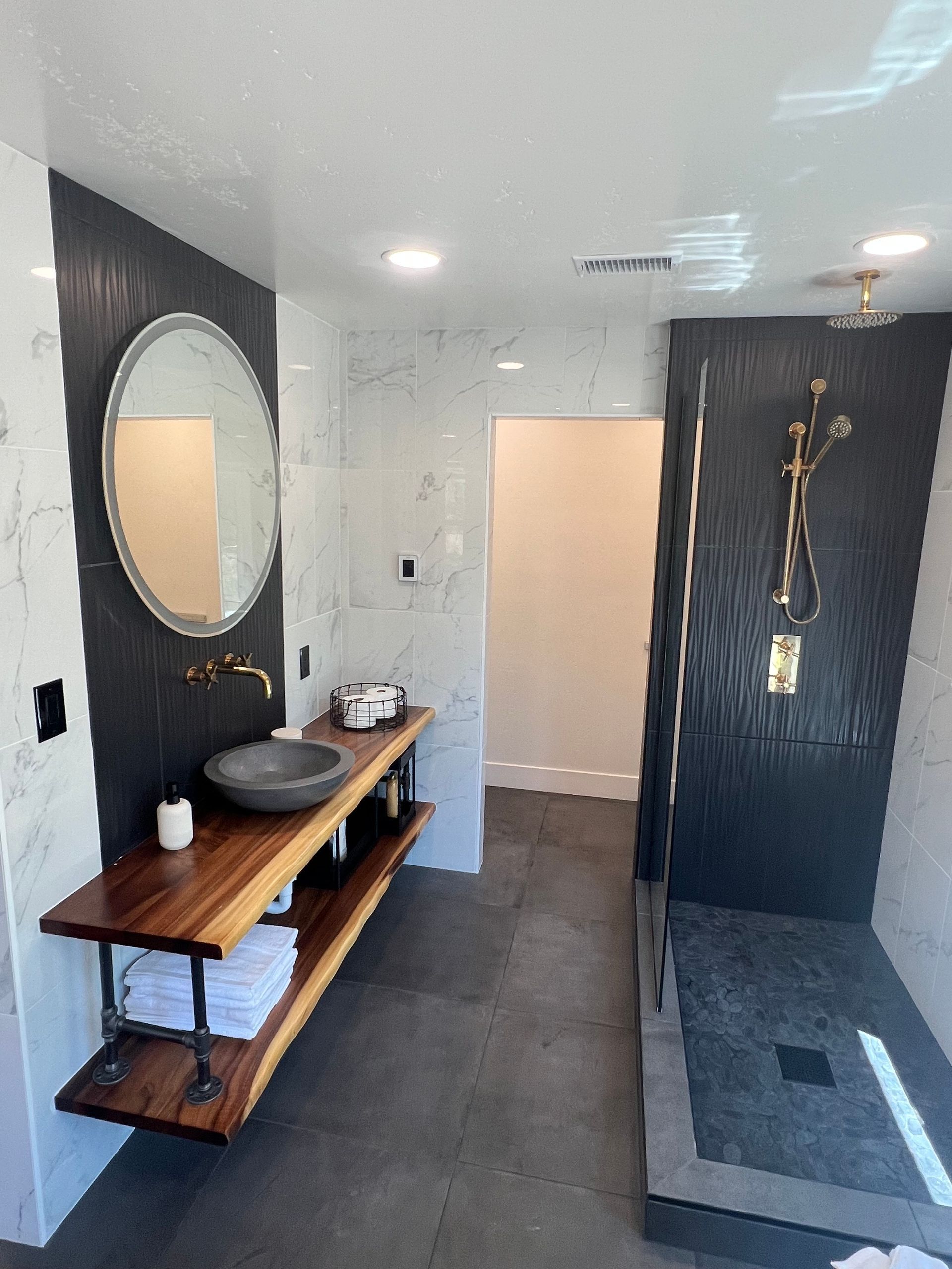 Modern bathroom with black and white tile, wooden vanity, and a walk-in shower.