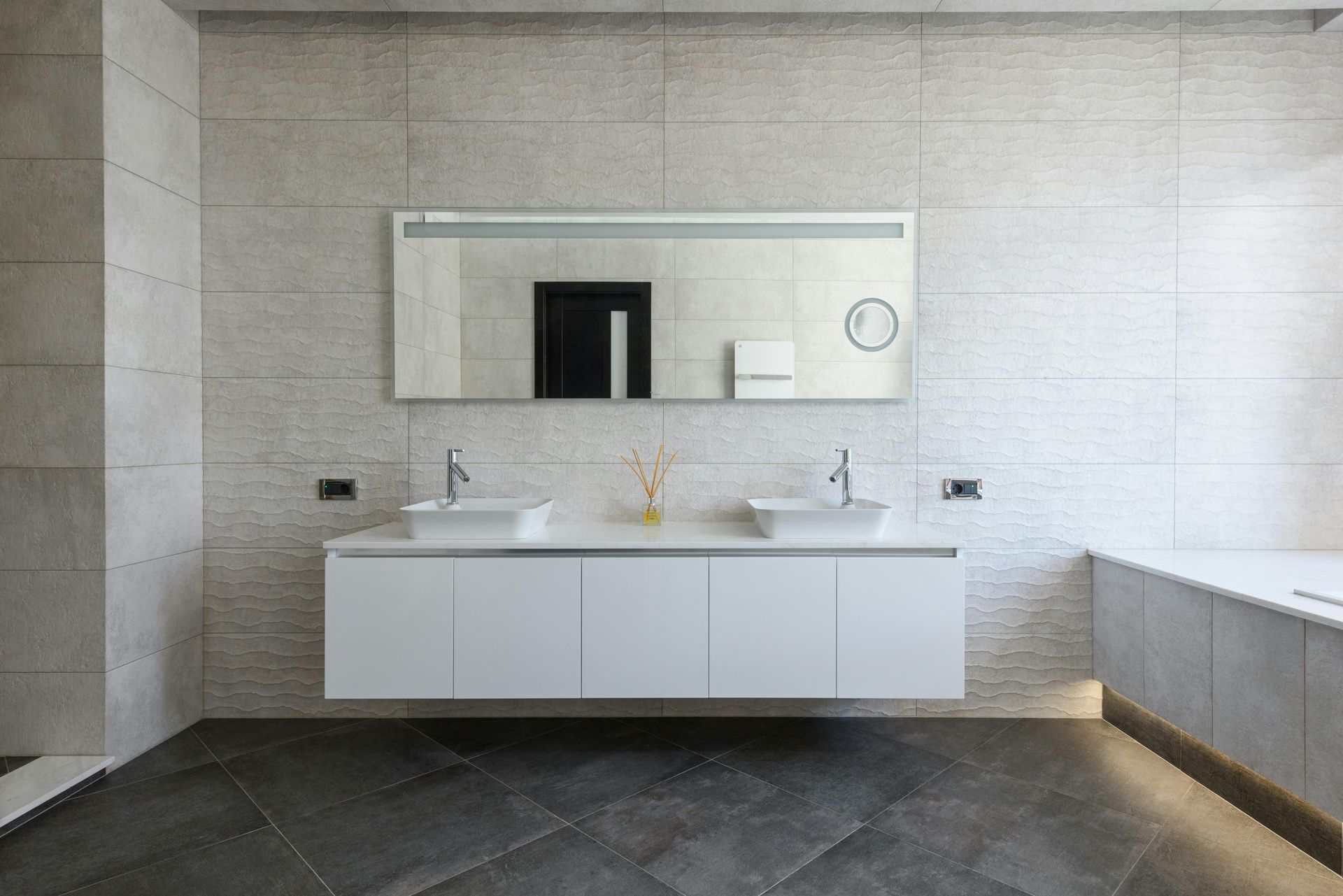 Modern bathroom with white floating vanity, double sinks, large mirror, and gray tiled walls and floor.