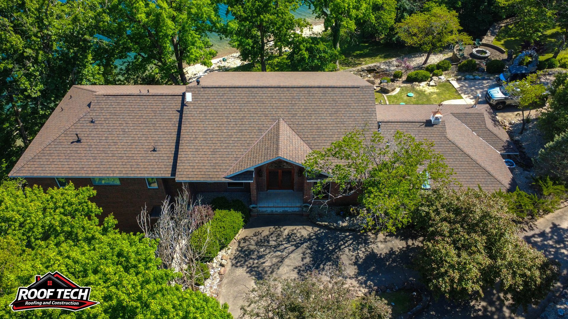 Aerial view of a brown-roofed house surrounded by lush green trees and a driveway