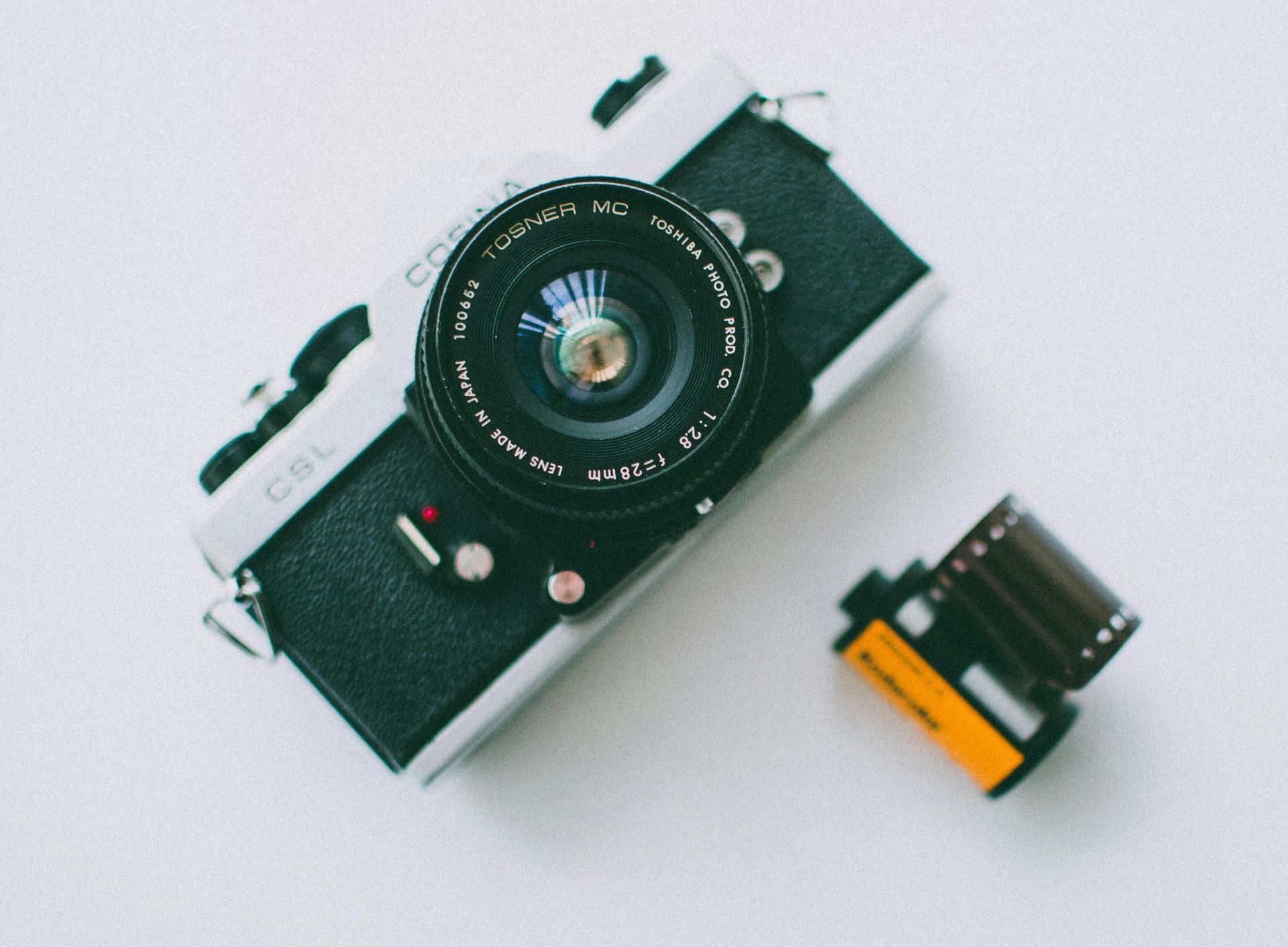 Vintage film camera next to a roll of film on a white surface.