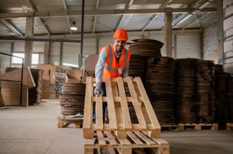 a man wearing a hard hat is stacking wooden pallets in a warehouse