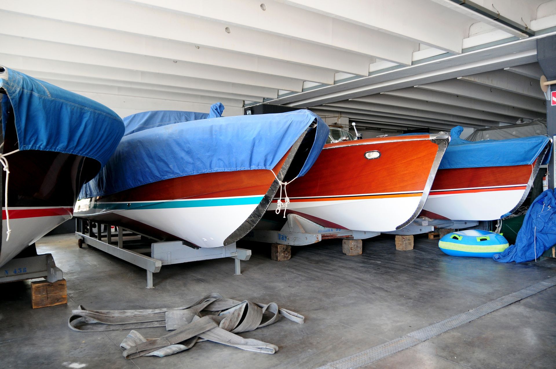 a row of boats are lined up in a warehouse and one of them has a blue cover on it