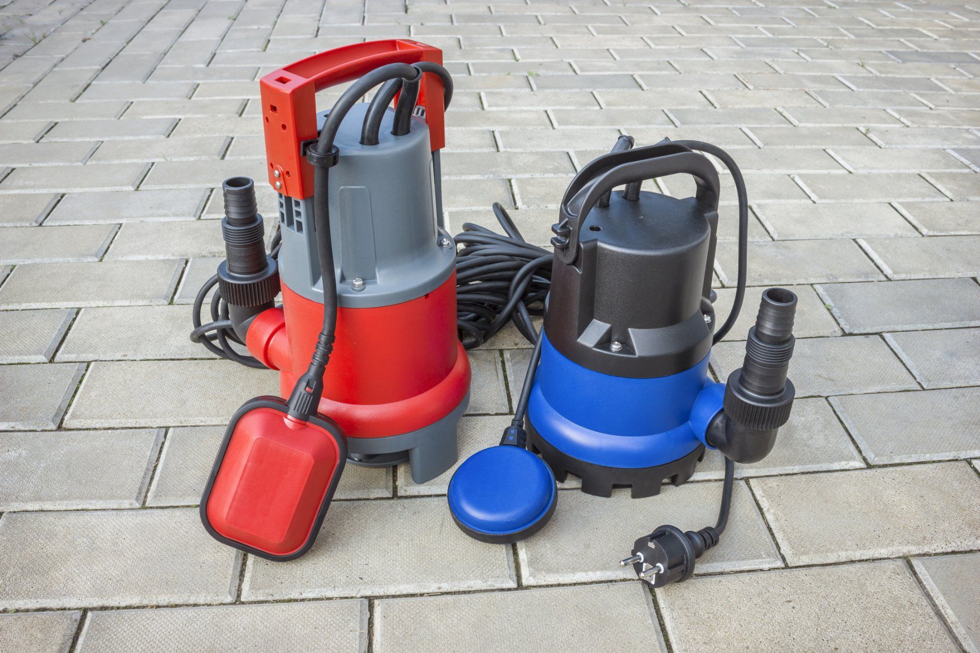 Two submersible pumps are sitting on a brick sidewalk.