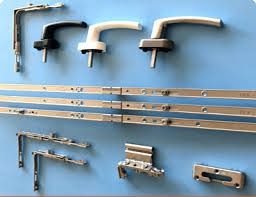 Componentes de hardware de ventanas sobre una superficie azul, incluidas manijas, bisagras y rieles.