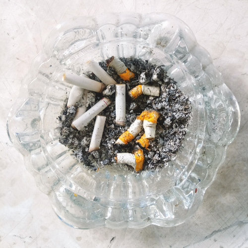A clear glass ashtray filled with cigarettes and ash