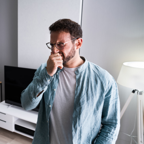 A man wearing glasses is coughing in a living room