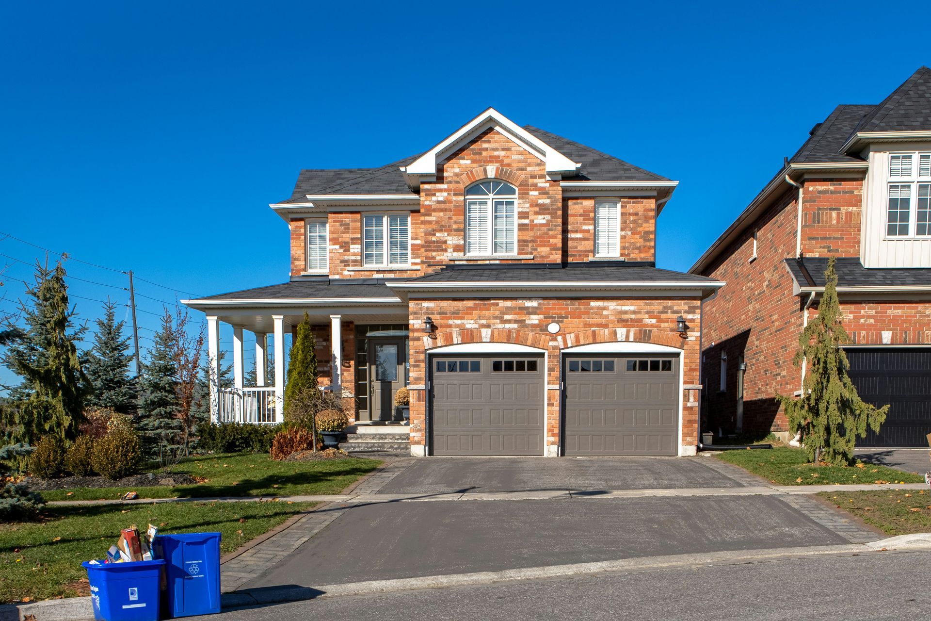 A large brick house with two garage doors and two blue trash cans in front of it