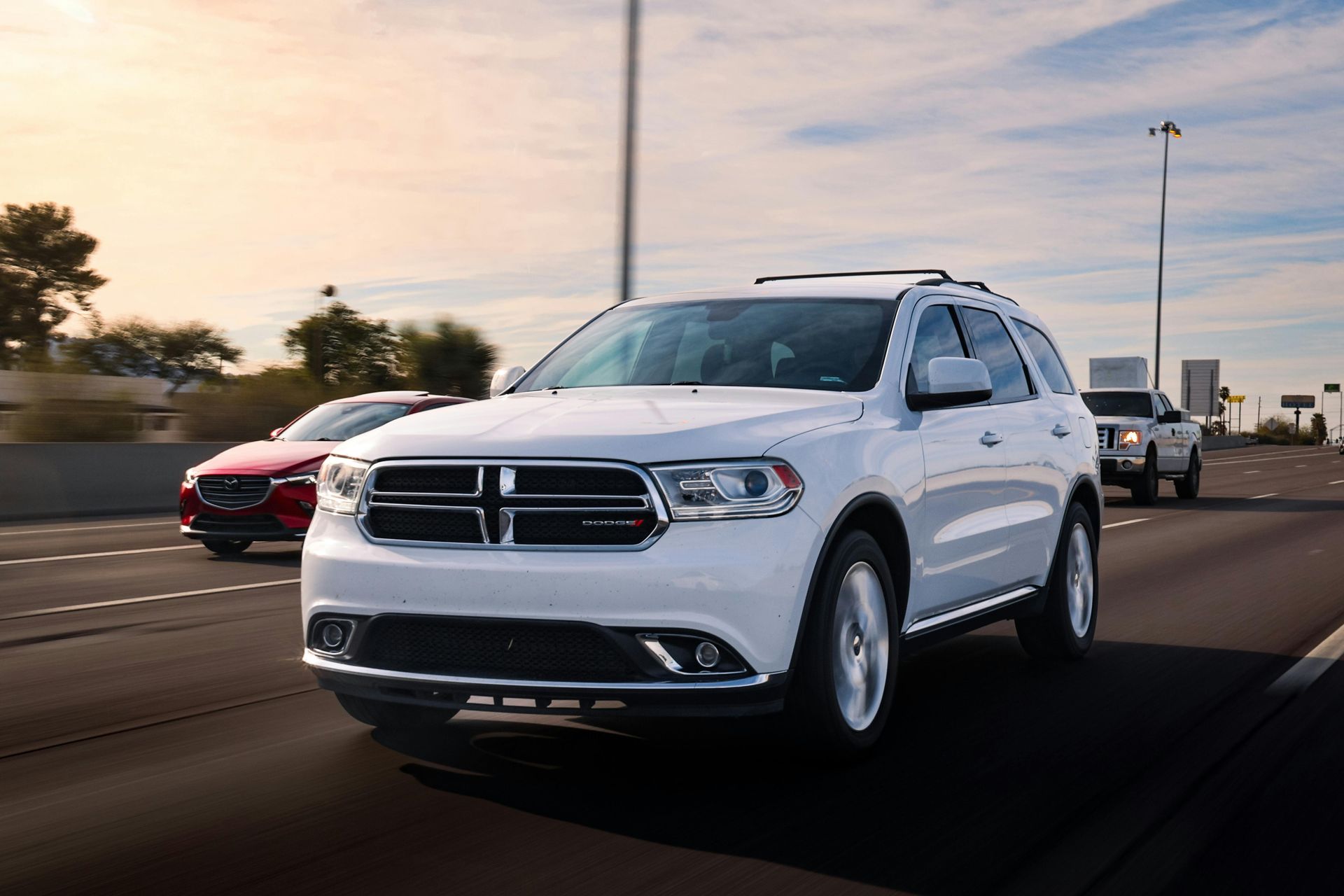 A white Dodge Durango driving on a highway during a bright, sunny day, with other cars in the background.