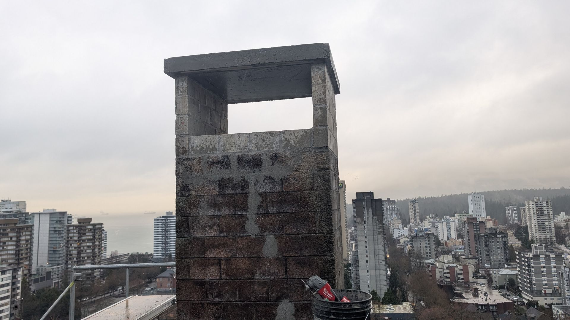 A repaired chimney on top of a building with a view of downtown Vancouver in the background.