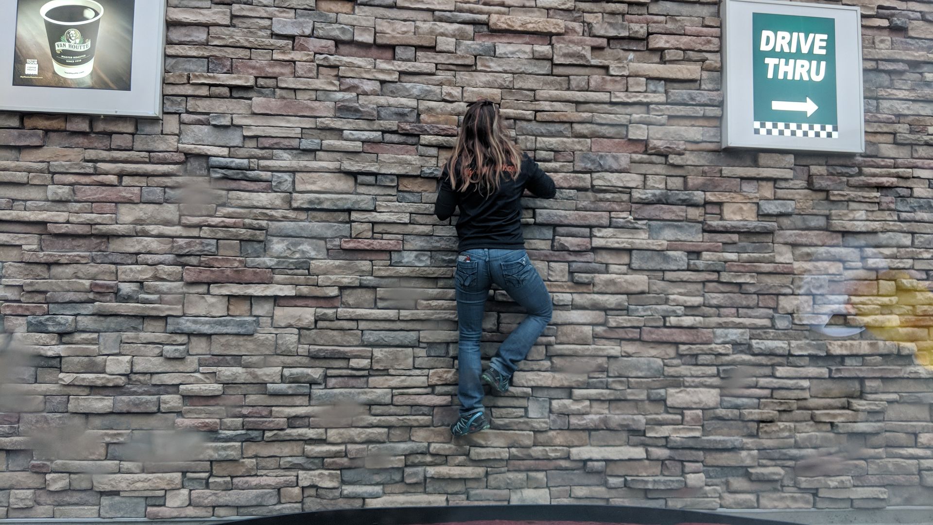 A masonry worker is climbing on a stone wall built by Bricked Masonry to show how strong it is.