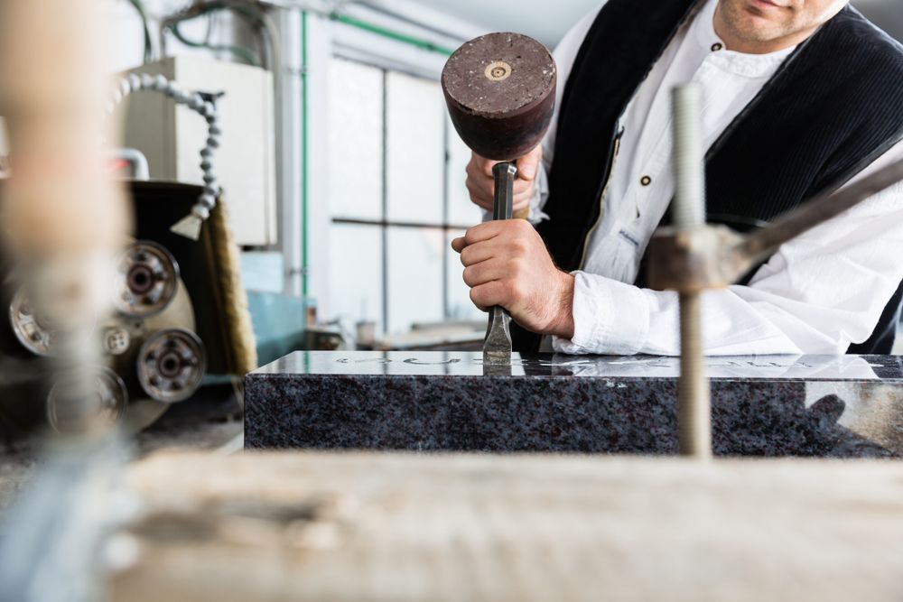 A man is holding a hammer over a piece of granite.