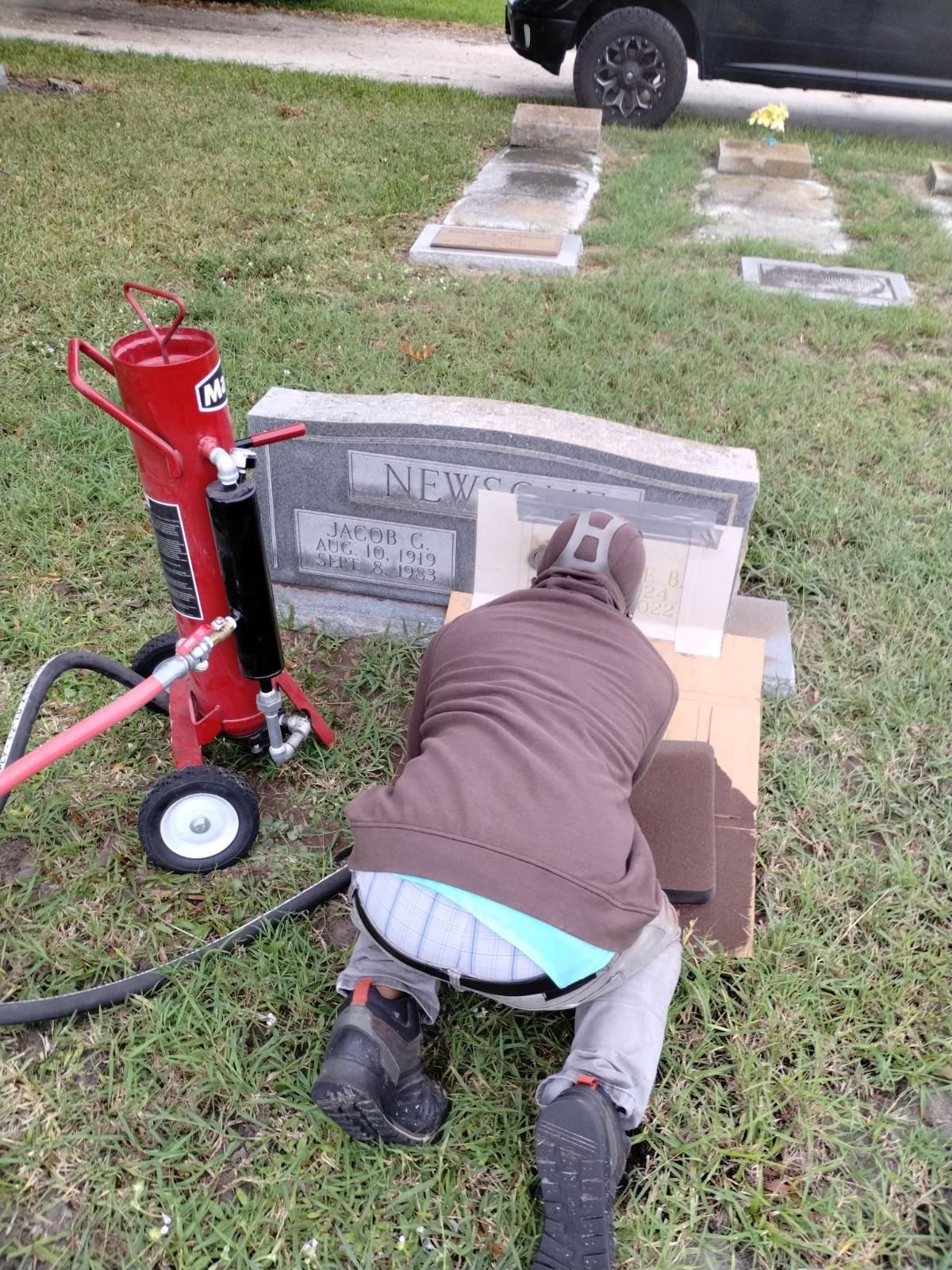 A man is kneeling down in front of a grave in a cemetery.