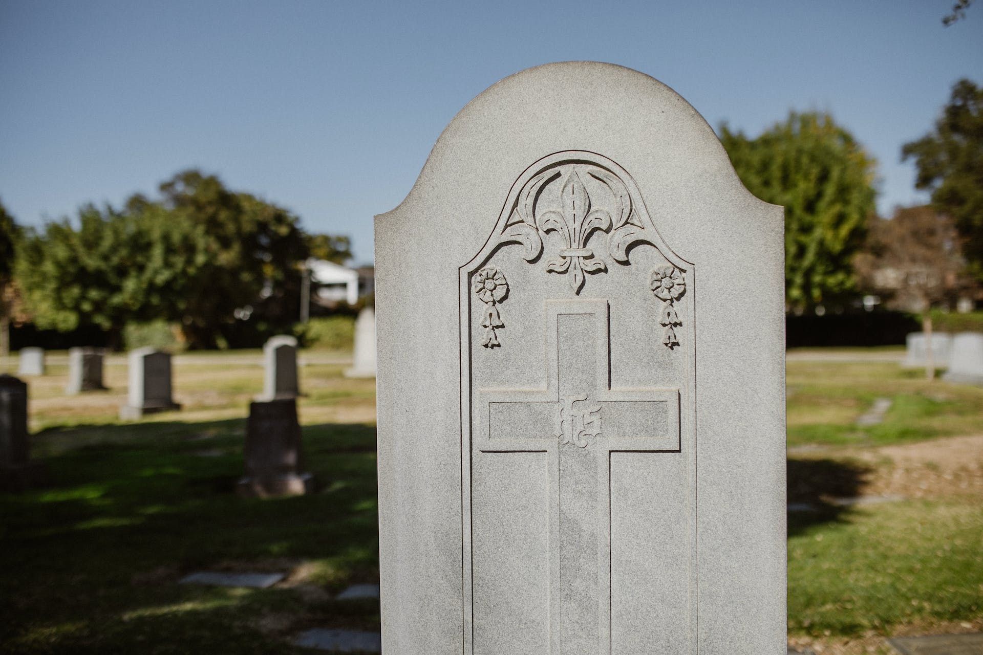 A gravestone with a cross carved into it is in a cemetery.