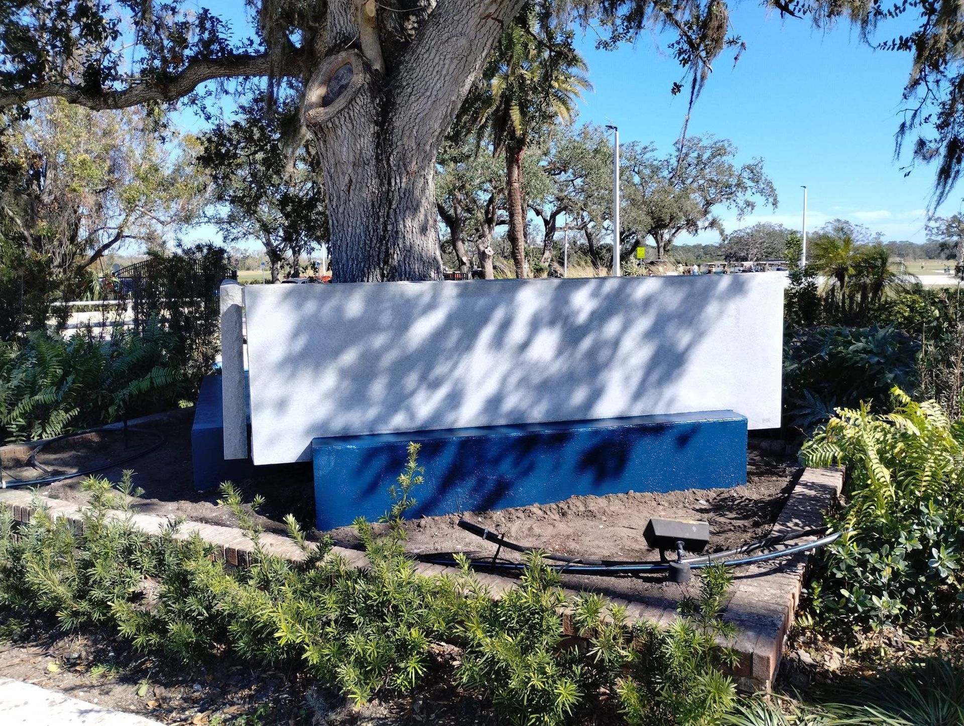 A white and blue sign is sitting under a tree
