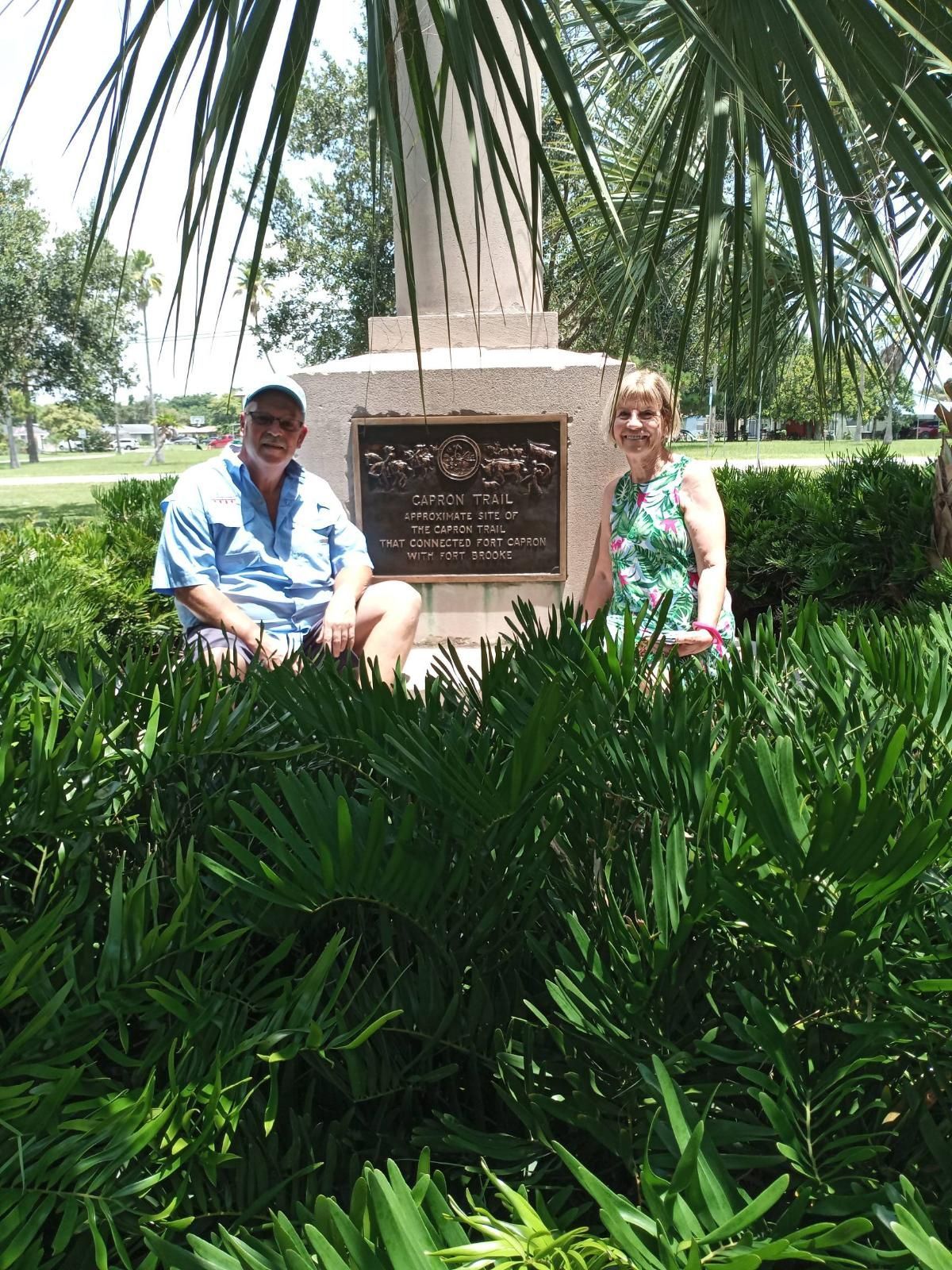 A man and a woman are standing in front of a statue in a park.